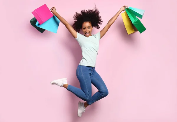 Porträt einer springenden afrikanisch-amerikanischen Frau mit Einkaufstüten auf farbigem Hintergrund — Stockfoto