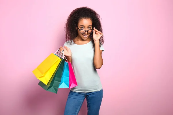 Portrait of beautiful African-American woman with shopping bags on color background — Stock Photo, Image