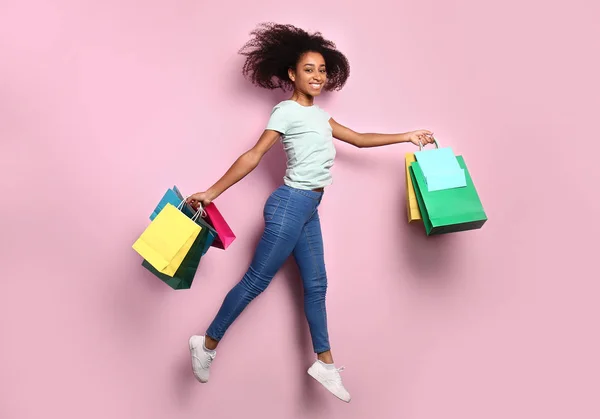 Jumping afro-amerikai nő, bevásárló táskák, színes háttér — Stock Fotó