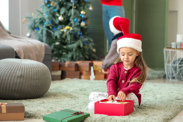 Nettes kleines Mädchen mit Geschenk und ihrer Familie zu Hause an Heiligabend — Stockfoto