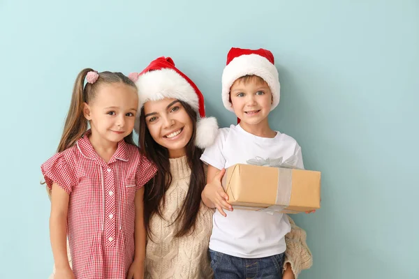 Frau und ihre kleinen Kinder mit Weihnachtsgeschenk auf farbigem Hintergrund — Stockfoto