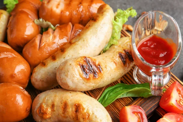 Tasty grilled sausages with sauce on wooden board, closeup — Stock Photo, Image