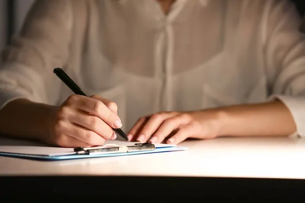 Женщина пишет что-то на листе бумаги на рабочем месте вечером, крупным планом — стоковое фото