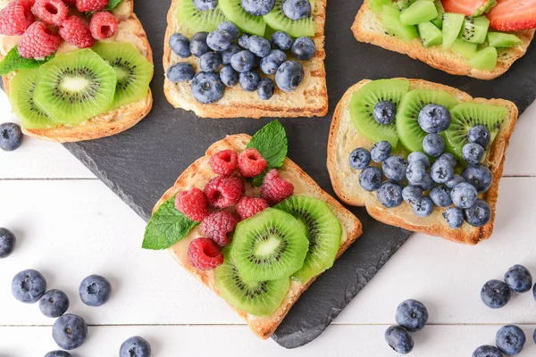 Beyaz masada lezzetli sandviçler, kivi ve çilek ile kayrak plaka