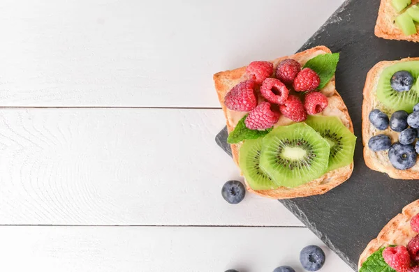 Assiette d'ardoise avec de savoureux sandwichs, kiwi et baies sur table blanche — Photo