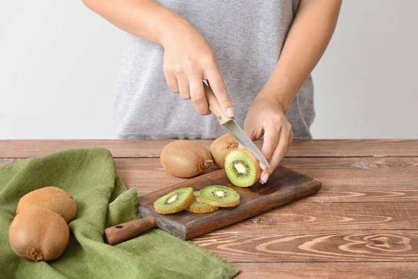 Woman cutting fresh kiwi at wooden table — Stock Photo, Image