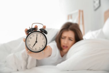 Yatak odasında çalar saat ile hoşnutsuz uykulu genç kadın Sabah