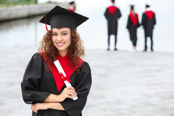 Šťastný afroamerický student bakalářského oblečení a s diplomem venku — Stock fotografie