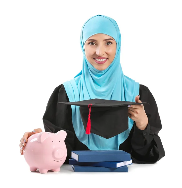 Mujer musulmana graduada con alcancía sobre fondo blanco. Concepto de tasas — Foto de Stock