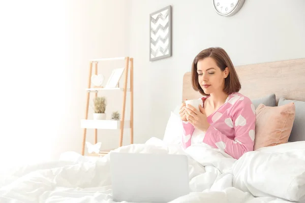 早晨美丽的年轻女子与笔记本电脑在床上喝咖啡 — 图库照片
