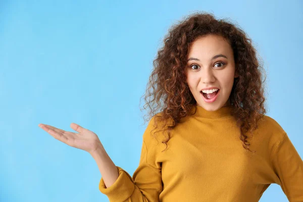 Surprised African-American woman showing something on color background — Stock Photo, Image