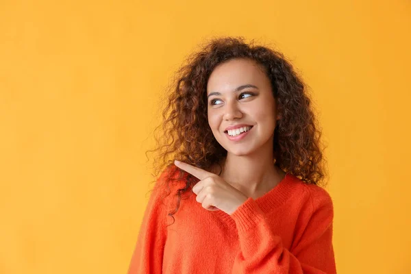 Beautiful African-American woman pointing at something on color background — Stock Photo, Image