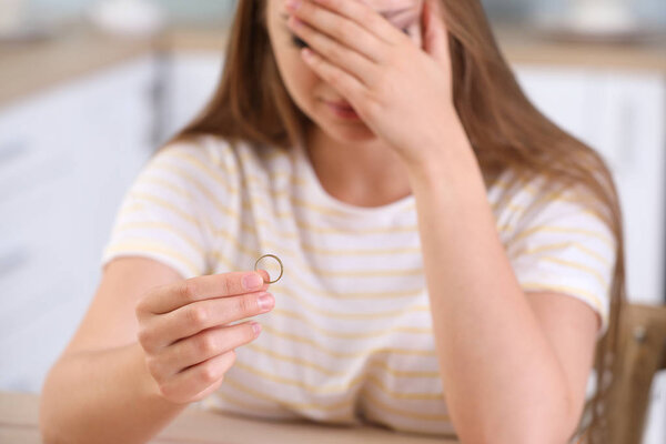 Upset woman with wedding ring at home. Concept of divorce