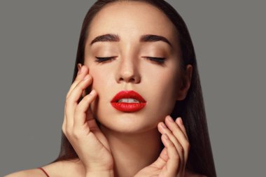 Gri arkaplanda parlak ruj izi olan güzel bir genç kadın.