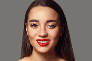 Gri arkaplanda parlak ruj izi olan güzel bir genç kadın.