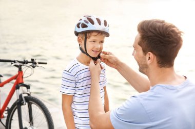 Baba dışarıda bisikletsürmeden önce kask koymak için oğlu yardım