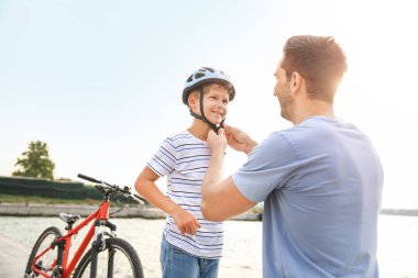 Baba dışarıda bisikletsürmeden önce kask koymak için oğlu yardım