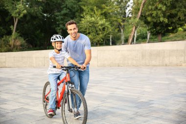 Baba oğluna dışarıda bisiklete binmeyi öğretiyor.