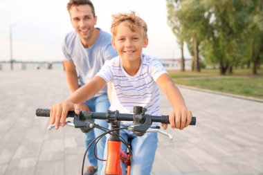 Baba oğluna dışarıda bisiklete binmeyi öğretiyor.