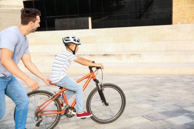 Baba oğluna dışarıda bisiklete binmeyi öğretiyor.
