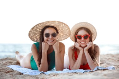 Güzel genç kadınlar tatil köyünde deniz kıyısında yatıyorlar.