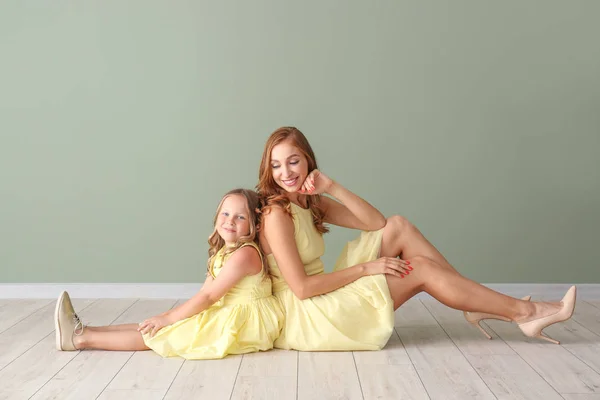 Beautiful woman and her little daughter sitting on floor near color wall — Stock Photo, Image