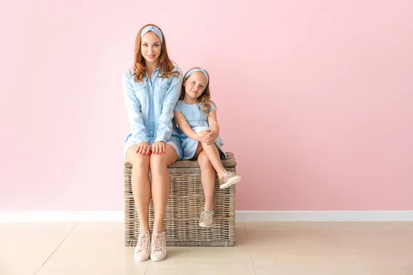 Beautiful woman and her little daughter sitting on wicker box near color wall — Stock Photo, Image