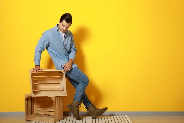 Stylish fashionable man and wooden boxes against color wall — Stock Photo, Image