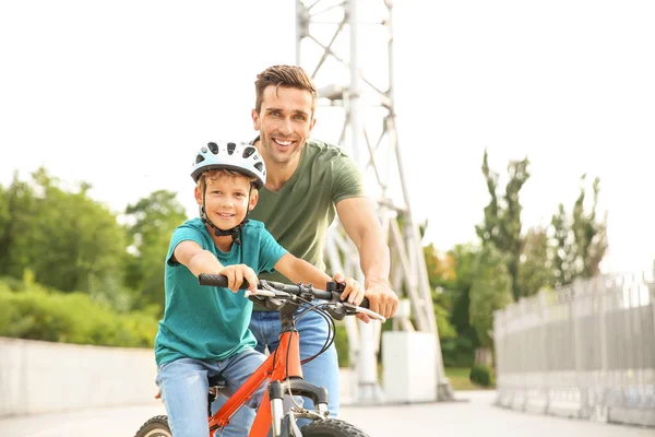 Padre enseñando a su pequeño hijo a andar en bicicleta al aire libre — Foto de Stock