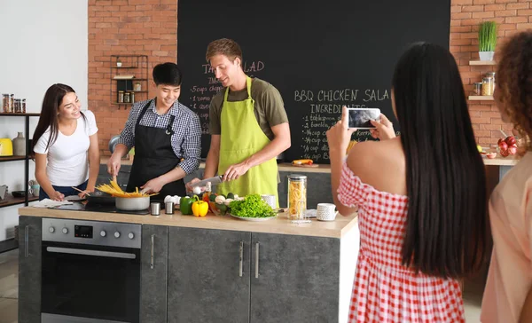 Азиатка фотографирует своих друзей, готовящих на кухне — стоковое фото