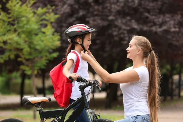 Mother helping her daughter to put on bicycle helmet outdoors