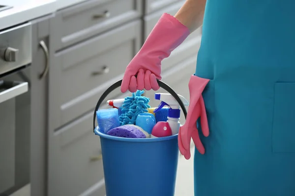 Mulher segurando balde com suprimentos de limpeza na cozinha, close-up — Fotografia de Stock