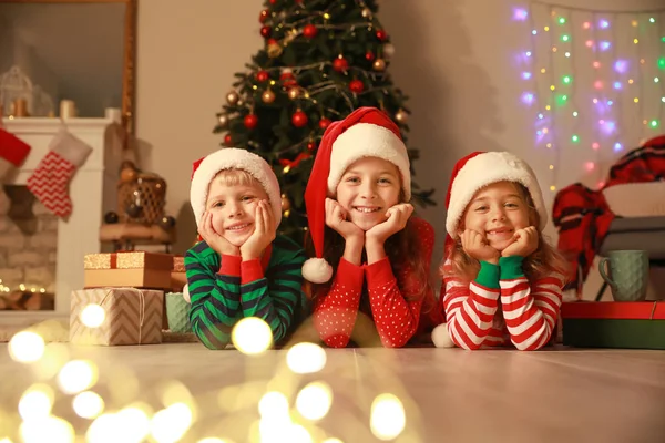 Niedliche kleine Kinder in Weihnachtsmannmützen liegen an Heiligabend zu Hause auf dem Boden — Stockfoto