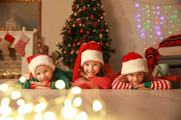 Söta små barn i Santa Claus hattar liggande på golvet på julafton hemma — Stockfoto