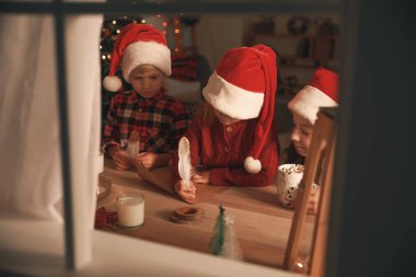 Noel arifesinde Noel Baba'ya evde mektup yazan sevimli küçük çocuklar. Pencereden görüntüle