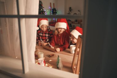 Noel arifesinde Noel Baba'ya evde mektup yazan sevimli küçük çocuklar. Pencereden görüntüle