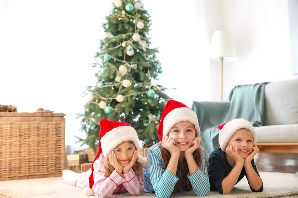 Niedliche kleine Kinder in Weihnachtsmannhüten, die zu Hause auf dem Boden liegen — Stockfoto