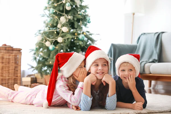 Gossiping little children in Santa Claus hats lying on floor at home — Stock Photo, Image