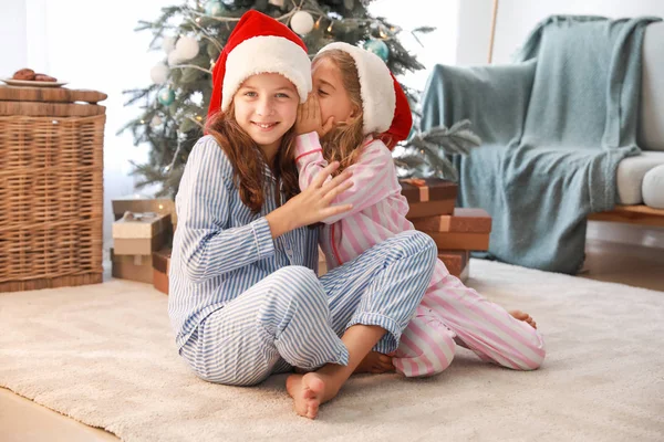 Chismes niñas en Santa Claus sombreros sentados en el suelo en casa — Foto de Stock