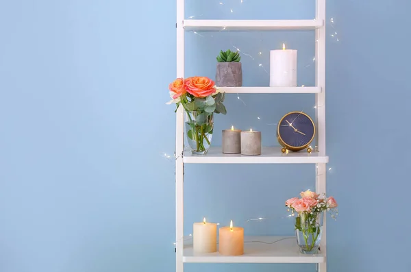 Brinnande ljus med rosa blommor på rack nära ljus vägg — Stockfoto