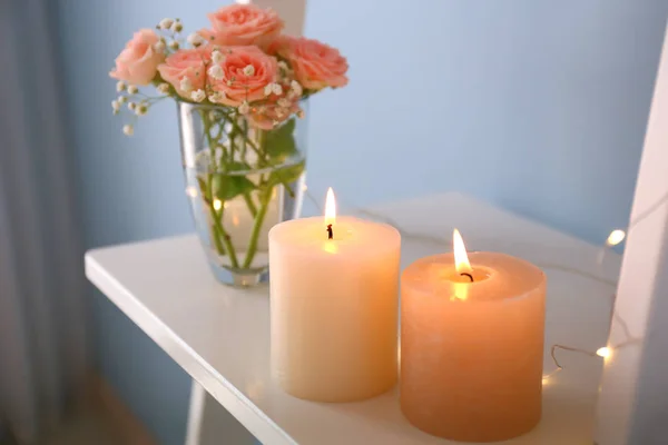 Горящие свечи с цветами роз на полке в помещении — стоковое фото