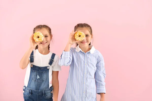 Portrait of happy twin girls with tasty donuts on color background — Stock Photo, Image