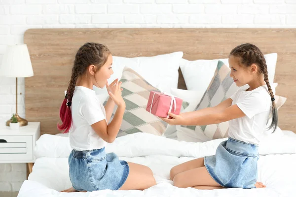Cute girl greeting her sister with gift in bedroom — Stock Photo, Image