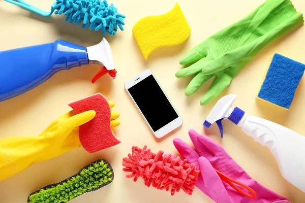 Cleaning supplies and mobile phone on color background