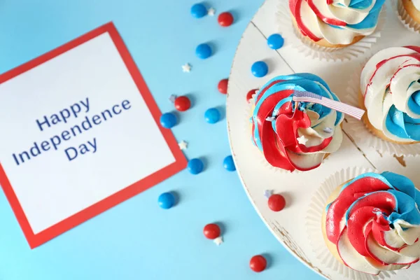 Cupcakes patrióticos saborosos e cartão com texto INDEPENDÊNCIA DE HAPPY DIA no fundo da cor — Fotografia de Stock