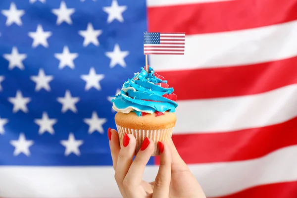 Female hand with tasty patriotic cupcake against USA flag — Stock Photo, Image