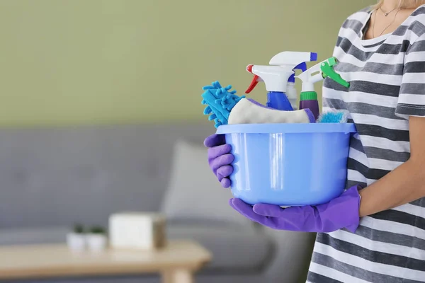 Mulher com conjunto de suprimentos de limpeza no quarto — Fotografia de Stock