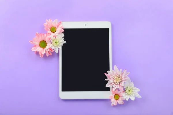 Modern tablet computer and flowers on color background