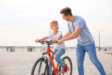 Baba oğluna dışarıda bisiklete binmeyi öğretiyor.