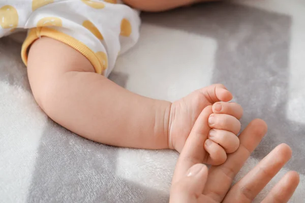 Hands of mother and cute little baby lying on bed, closeup — Stock Photo, Image